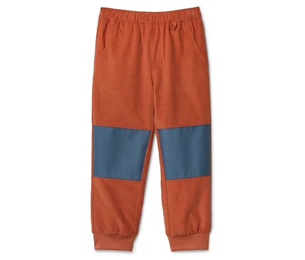 Orangefarbene Cordhose mit blauen Kniepatches liegt auf einem weißen Hintergrund.