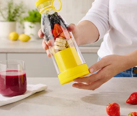 Eine Frau hält eine durchsichtige Flasche mit gelben Akzenten, gefüllt mit Bananen, Erdbeeren und Blaubeeren.