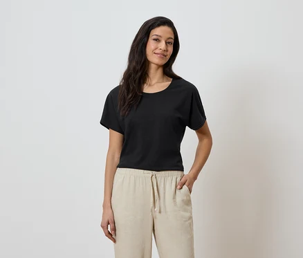 Frau mit schwarzem T-Shirt und beiger Hose mit der Hand in der Hosentasche.
