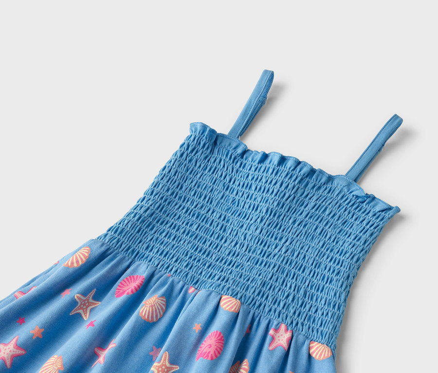 Detailaufnahme eines blauen Sommerkleides mit elastischem Oberteil und Trägern, bedruckt mit rosa und orangefarbenen Muscheln und Seesternen.