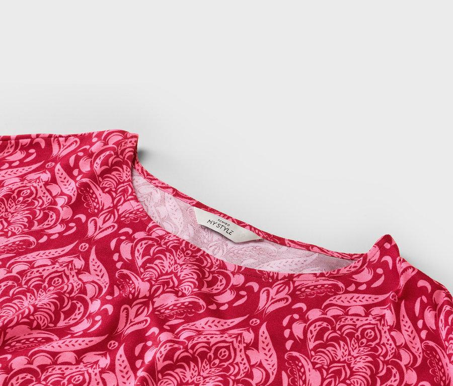 Nahaufnahme des Ausschnitts eines rot-pink gemusterten Oberteils mit einem 'TCHIBO MY STYLE'-Etikett.