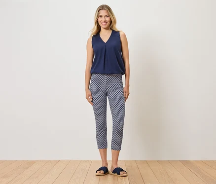 Frau steht und trägt ein blaues Top, gemusterte Hose und blaue Hausschuhe.