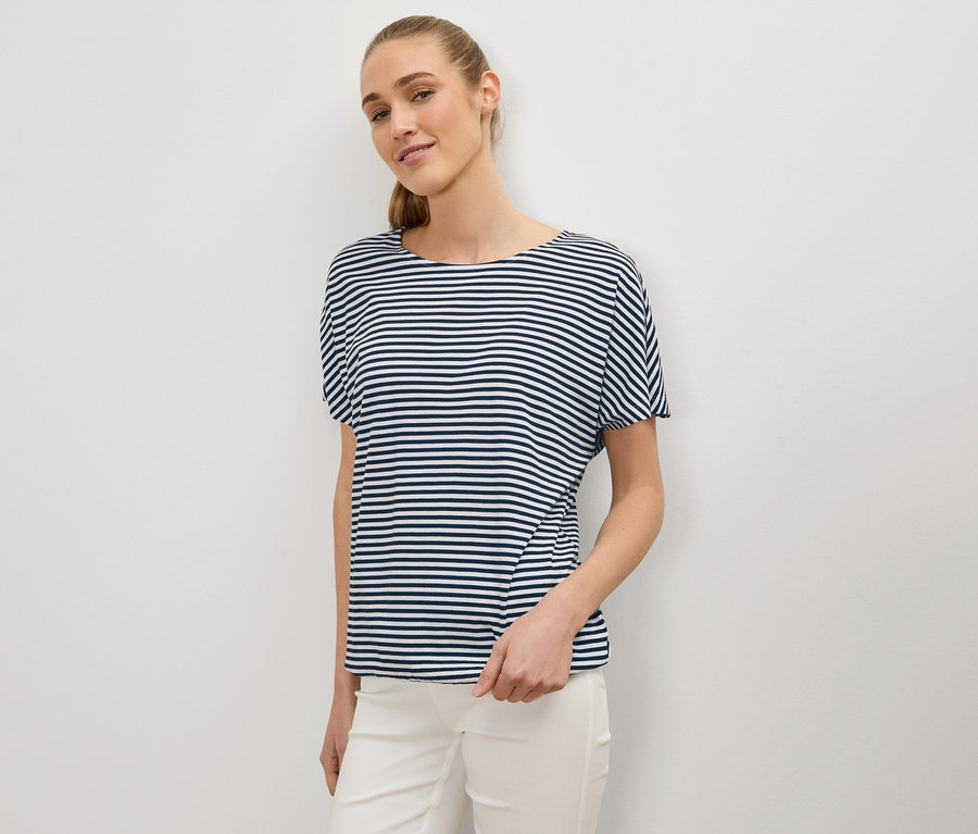 Frau mit Pferdeschwanz trägt ein blau-weiß gestreiftes T-Shirt und weiße Hose.