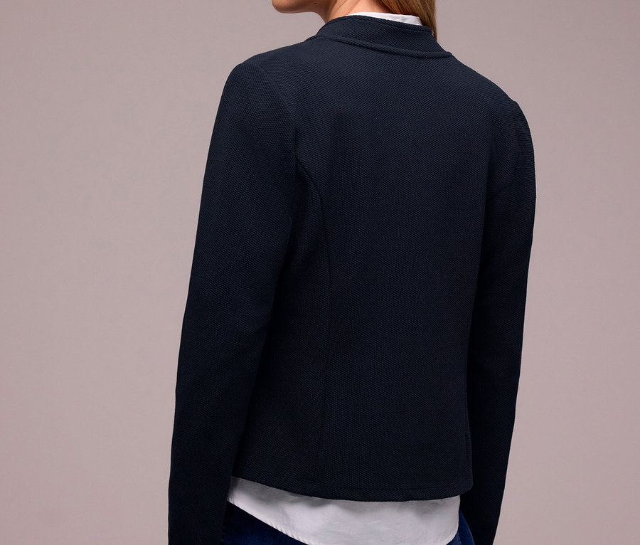 Frau von hinten, leicht nach rechts gedreht, trägt einen dunkelblauen Street One Jerseyblazer über einem weißen Hemd und blauen Jeans.
