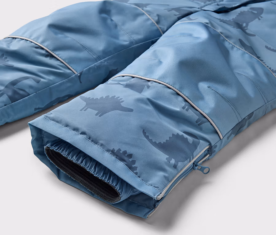 Nahaufnahme der Unterseite einer blauen Hose mit Dinosaurier-Muster und Reißverschluss am Bein.