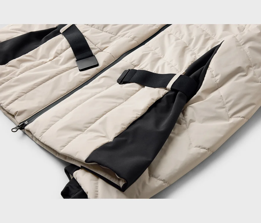 Nahaufnahme einer beigefarbenen Steppjacke mit schwarzen Stoffeinsätzen und schwarzen Riemen mit Schnallen.