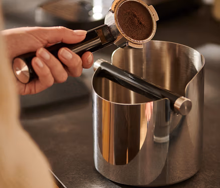 Hand hält Kaffeeträger über glänzender Knock Box.