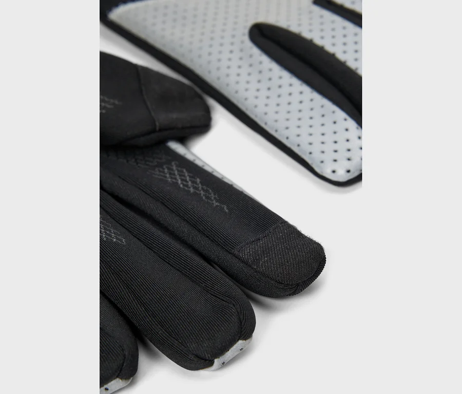 Nahaufnahme von schwarzen Handschuhen mit hellgrauen, perforierten Handflächen und gerippten Fingern, die ein dezentes Muster auf dem Handrücken zeigen.