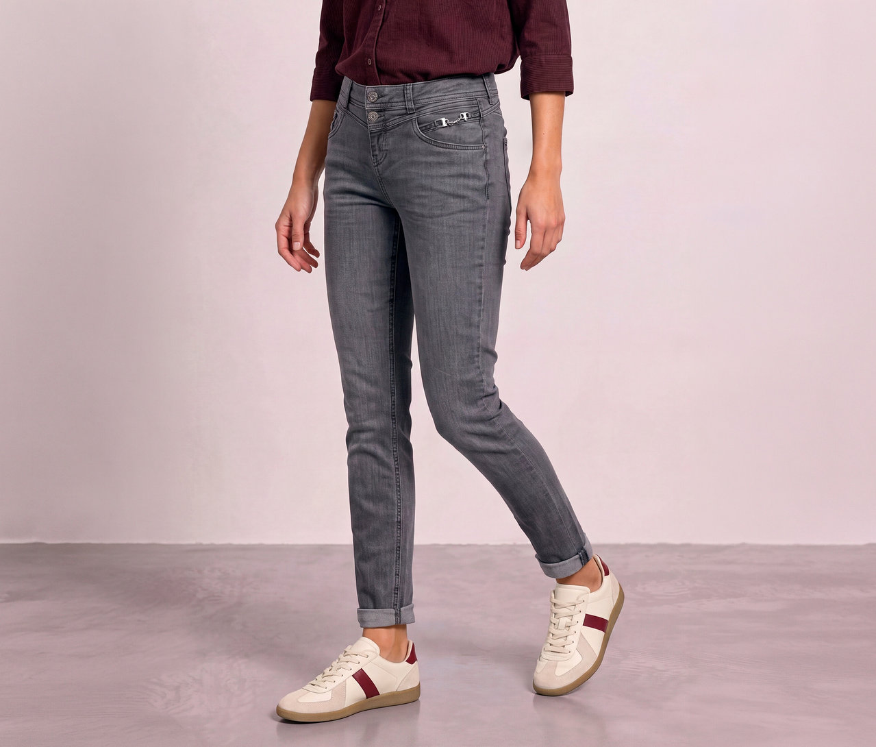 Person trägt graue Street One Jeans mit hochgekrempelten Knöcheln und cremefarbene Sneaker mit bordeauxroten Streifen.
