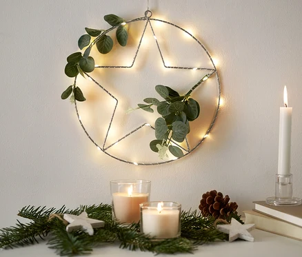 Ein LED-Ring mit künstlichen Zweigen hängt an der Wand. Auf der Kommode liegen Kerzen und Zweige.
