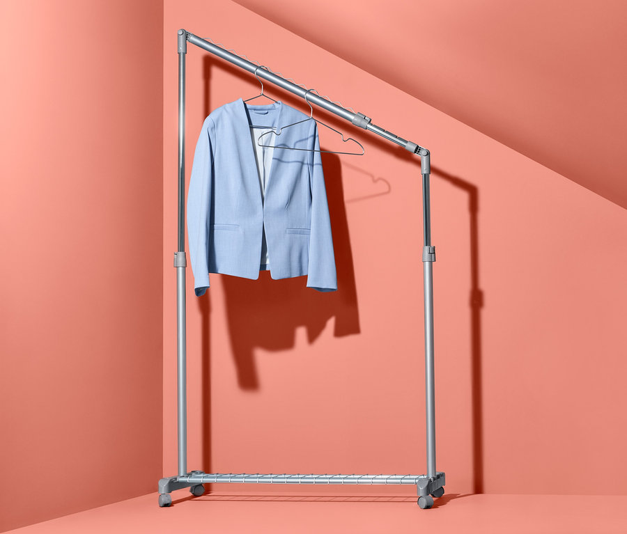 Ein hellblauer Blazer hängt auf einem höhenverstellbaren Kleiderständer in einer Ecke des Zimmers.
