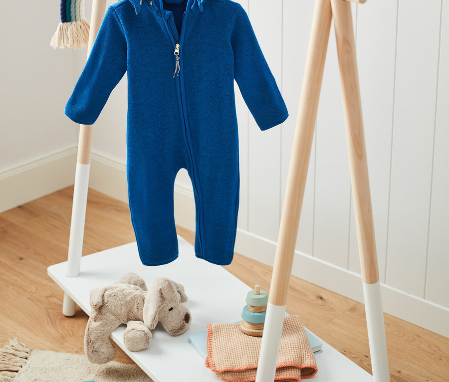 Blauer Strickfleece-Einteiler mit Kapuze mit recyceltem Material hängt auf einem Holzständer.