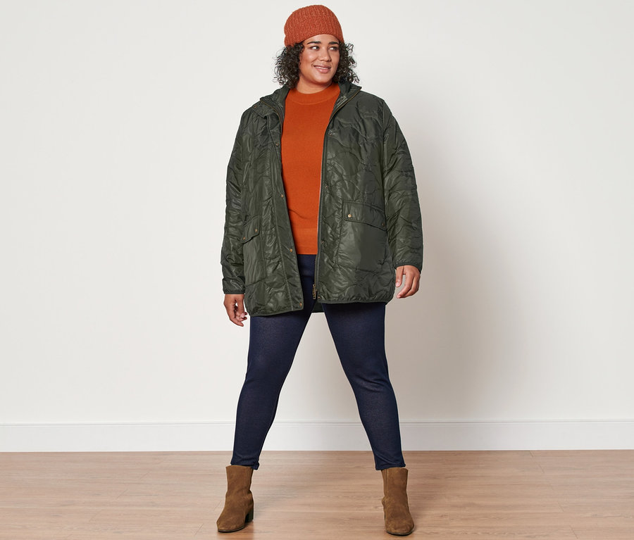 Frau posiert in Strickpullover, Steppjacke, gefütterten Leggings in Jeansoptik, Strickmütze und Stiefeletten aus Veloursleder für die Kamera.