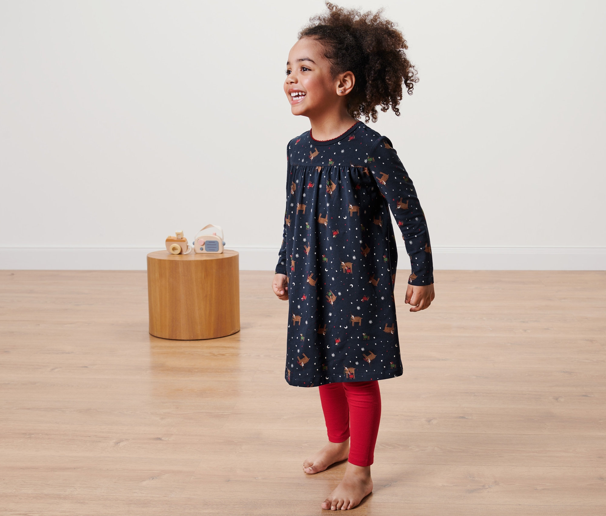 Ein lächelndes kleines Mädchen trägt ein Kleinkind-Nachthemd mit Leggings.