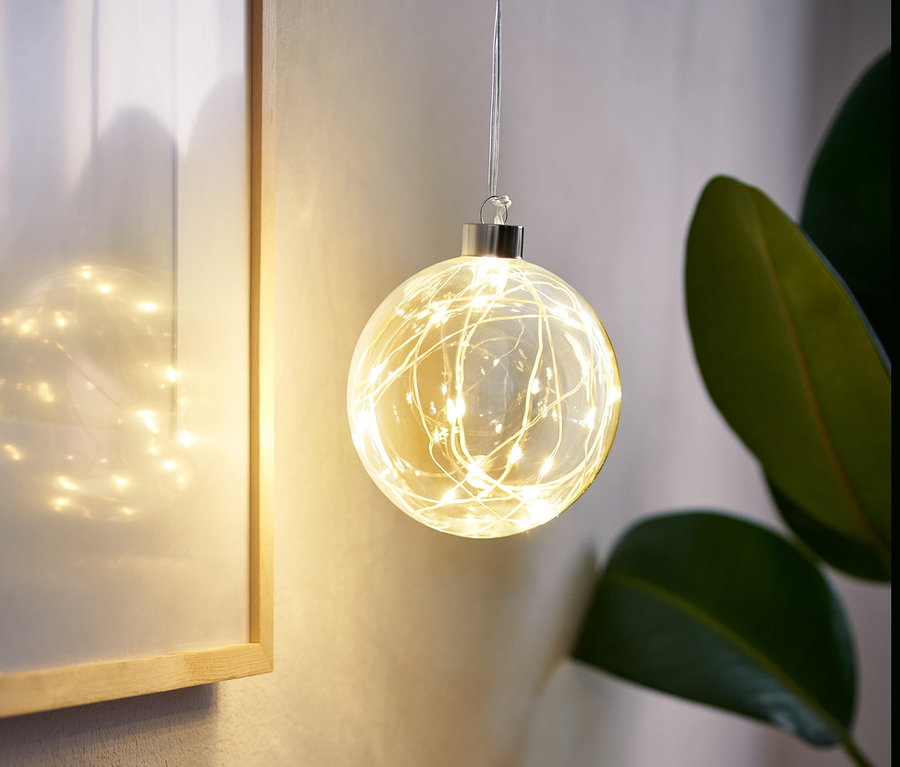 Eine LED-Glaskugel hängt im Raum, daneben ein gerahmtes Bild und eine Vase mit Gras.