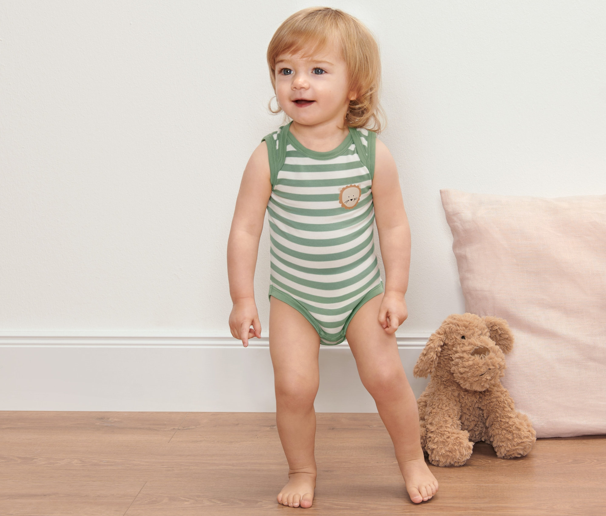 Kleinkind steht auf dem Boden und trägt 2 Baby-Bodys mit Mitwachsfunktion.