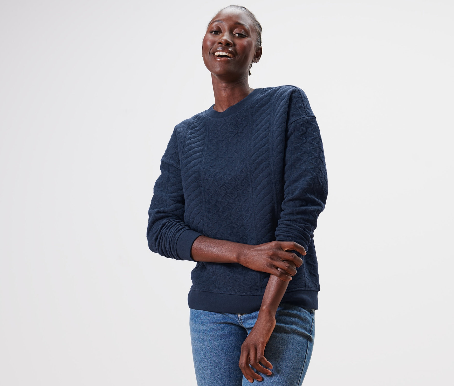 Frau trägt ein blaues Sweatshirt mit Zopfmuster und Jeans.