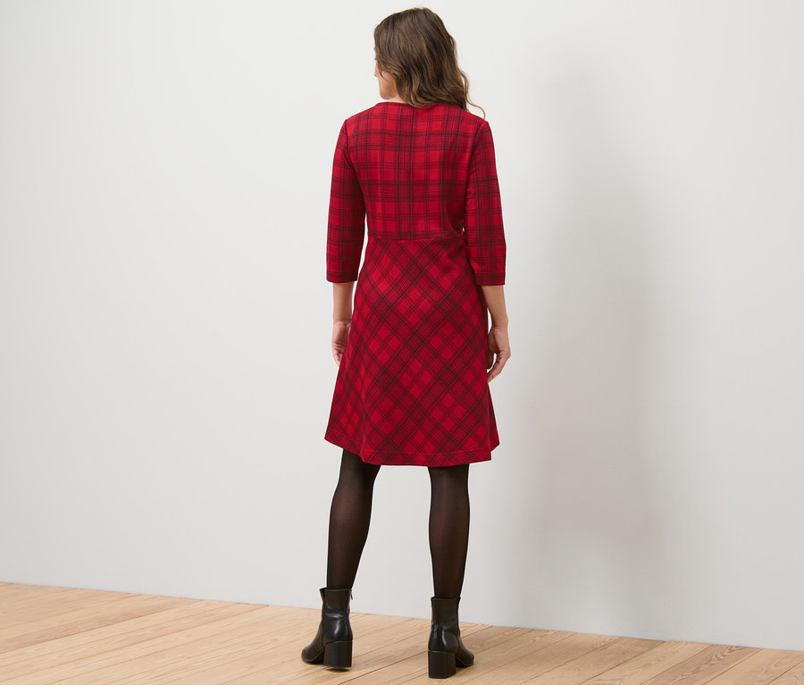 Frau von hinten in einem karierten Jacquard-Kleid, einer schwarzen Strumpfhose und schwarzen Stiefeln.