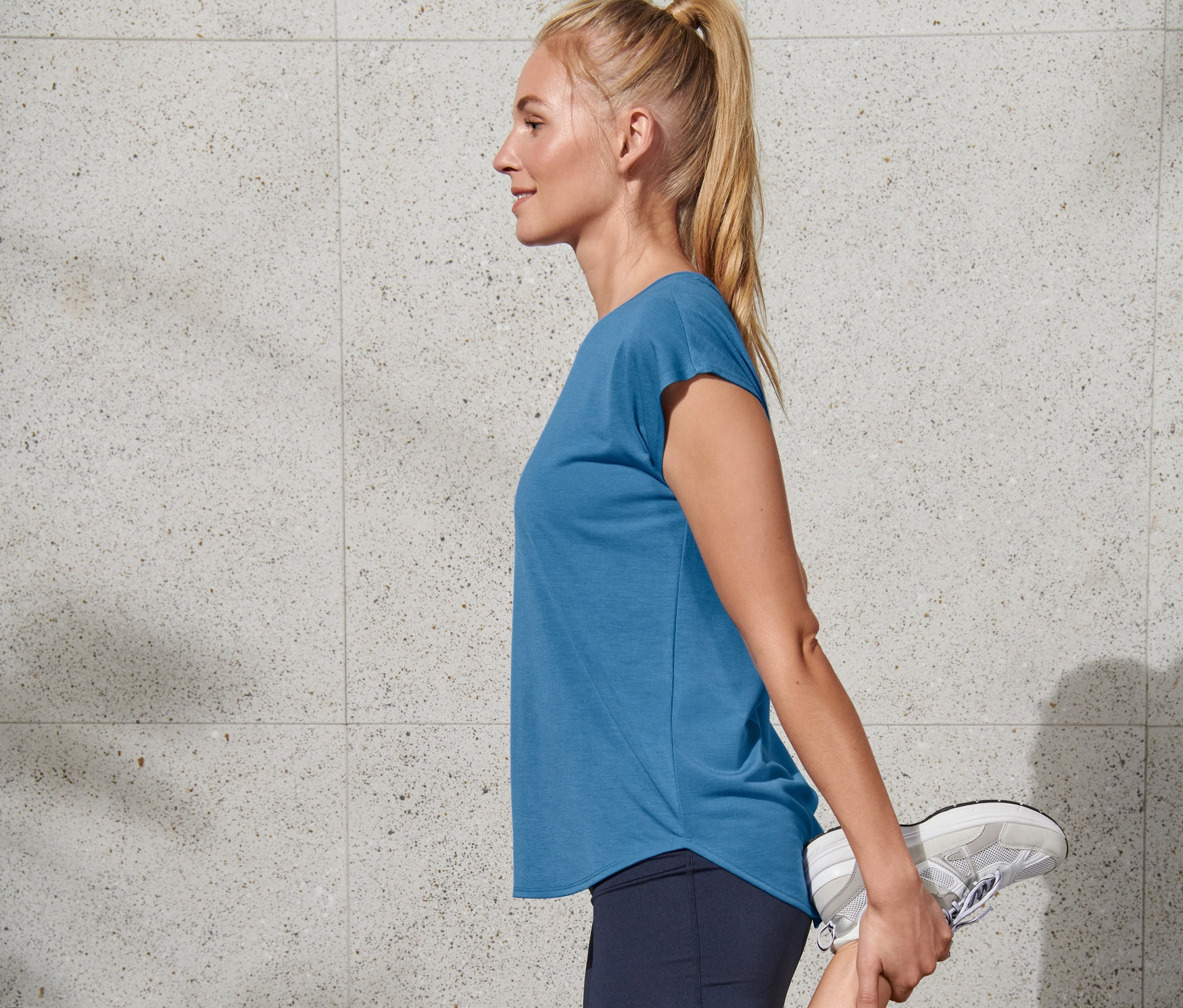 Blonde Frau dehnt ihr Bein, trägt ein blaues Sportshirt von Regatta.
