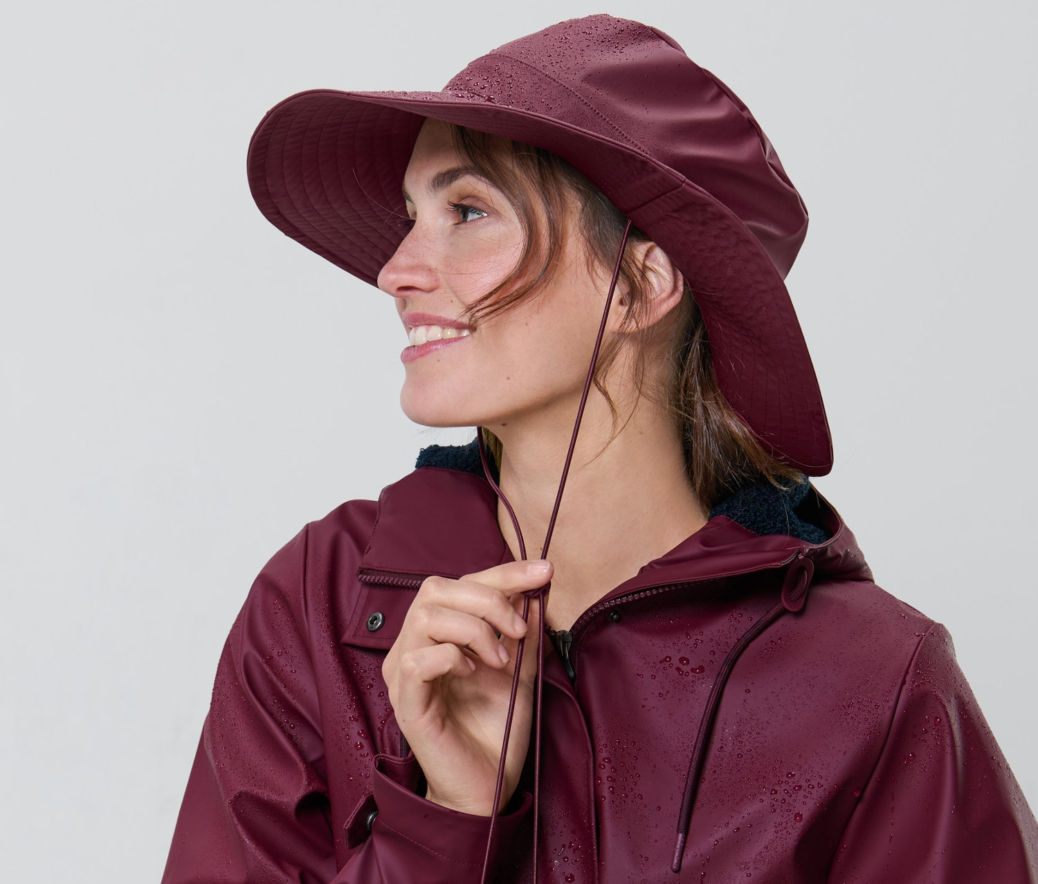 Frau reguliert die Schnur an einem weinroten Regenhut.