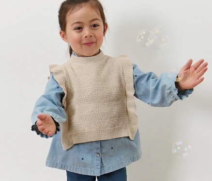 Mädchen in Kinder-Strickpullunder posiert mit ausgestreckten Armen.