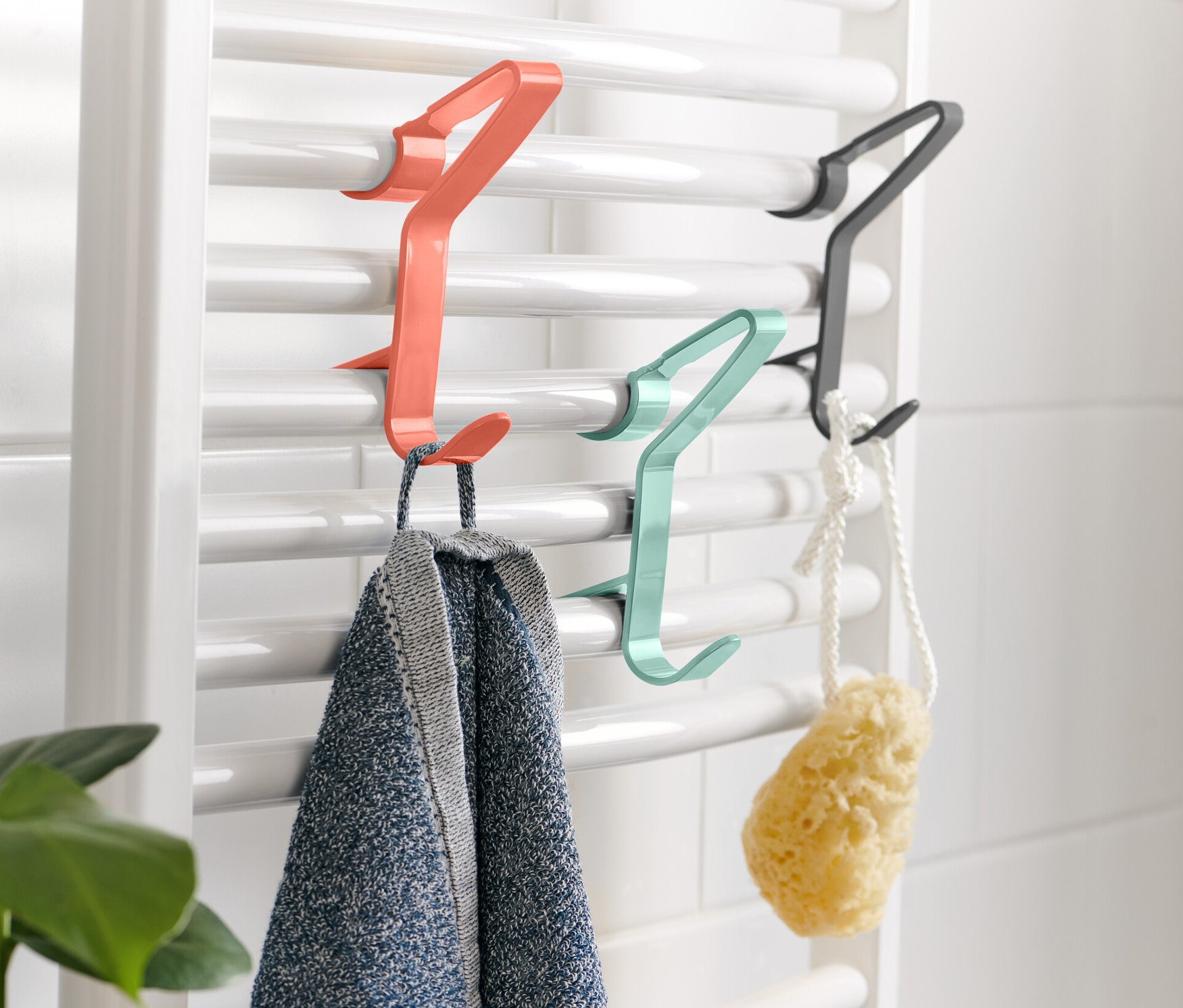 An einer weißen Heizung hängen 3 Heizkörper-Haken, an denen ein Handtuch und ein Schwamm hängen.