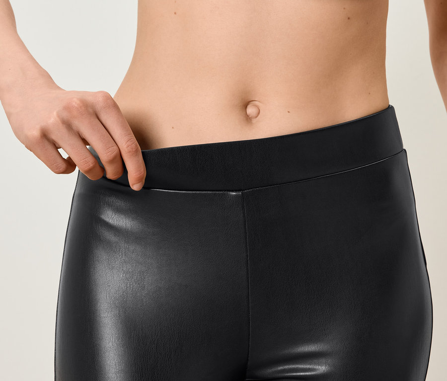Detailaufnahme einer Frau, die den Bund einer schwarzen Leggings aus Kunstleder hält.