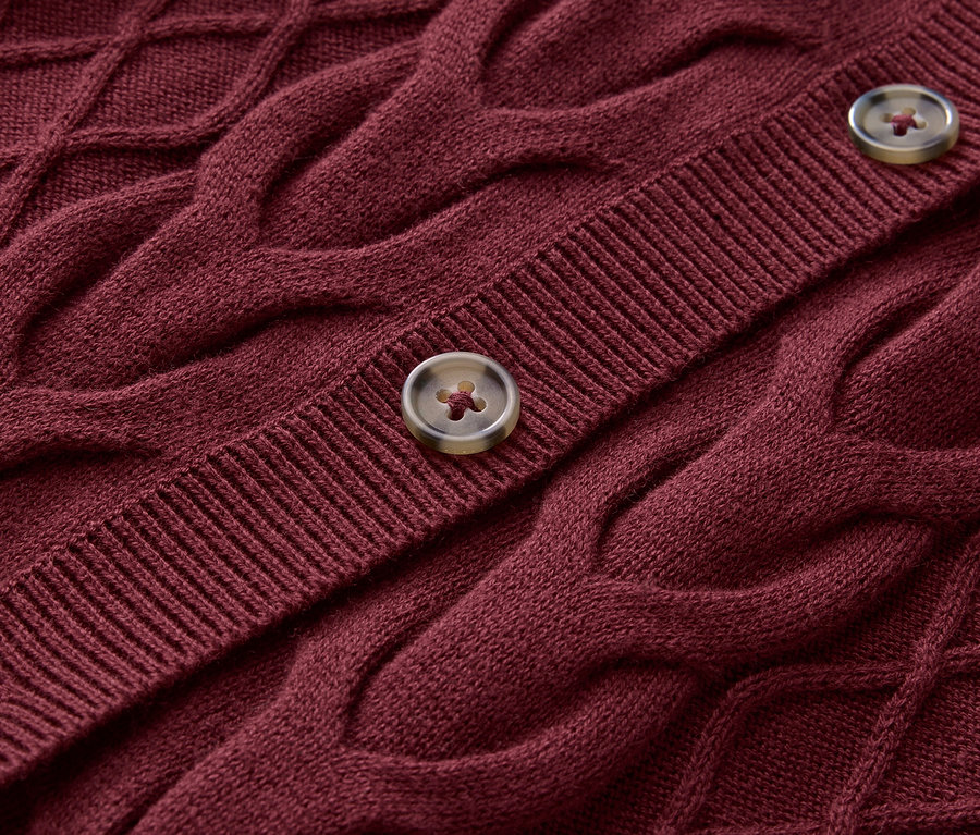 Detailaufnahme eines bordeauxroten Strickpullovers mit Zopfmuster und zwei Knöpfen.