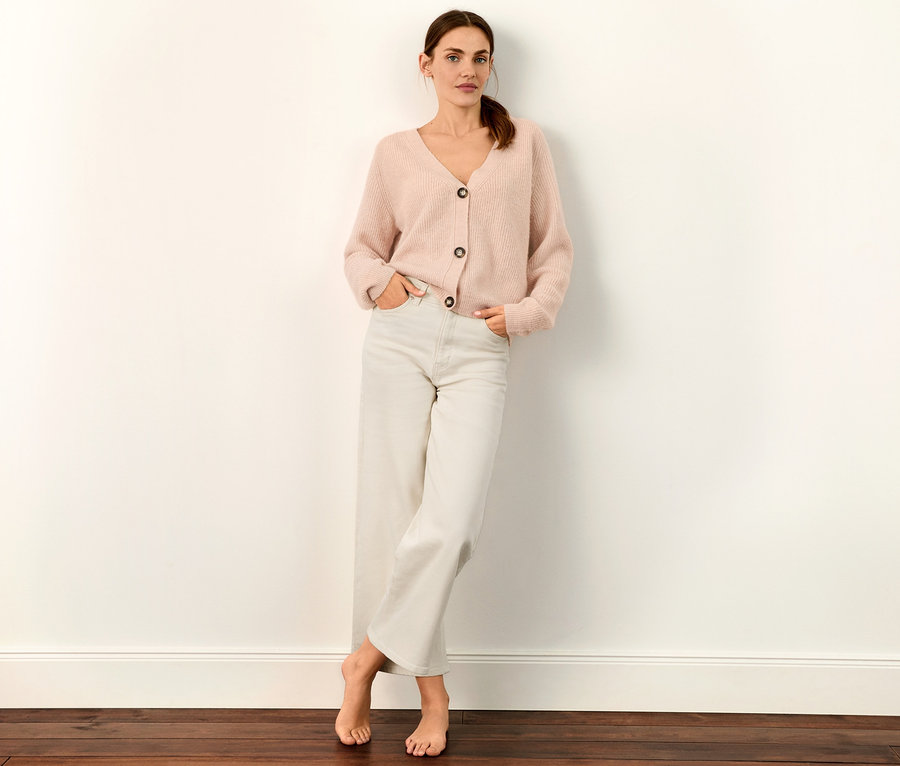 Frau posiert in weißer Culotte-Jeans und rosa Strickjacke.