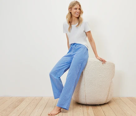 Blonde Frau sitzt in einem Pyjama-Set auf einem Pouf.
