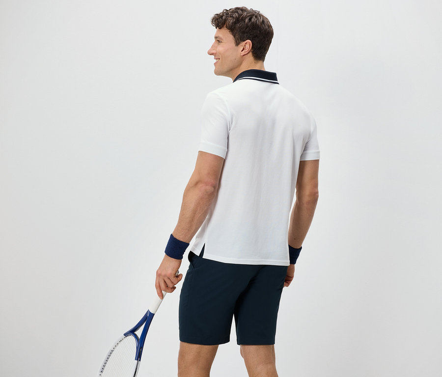 Mann von hinten hält Tennisschläger und trägt ein weißes Funktions-Poloshirt.