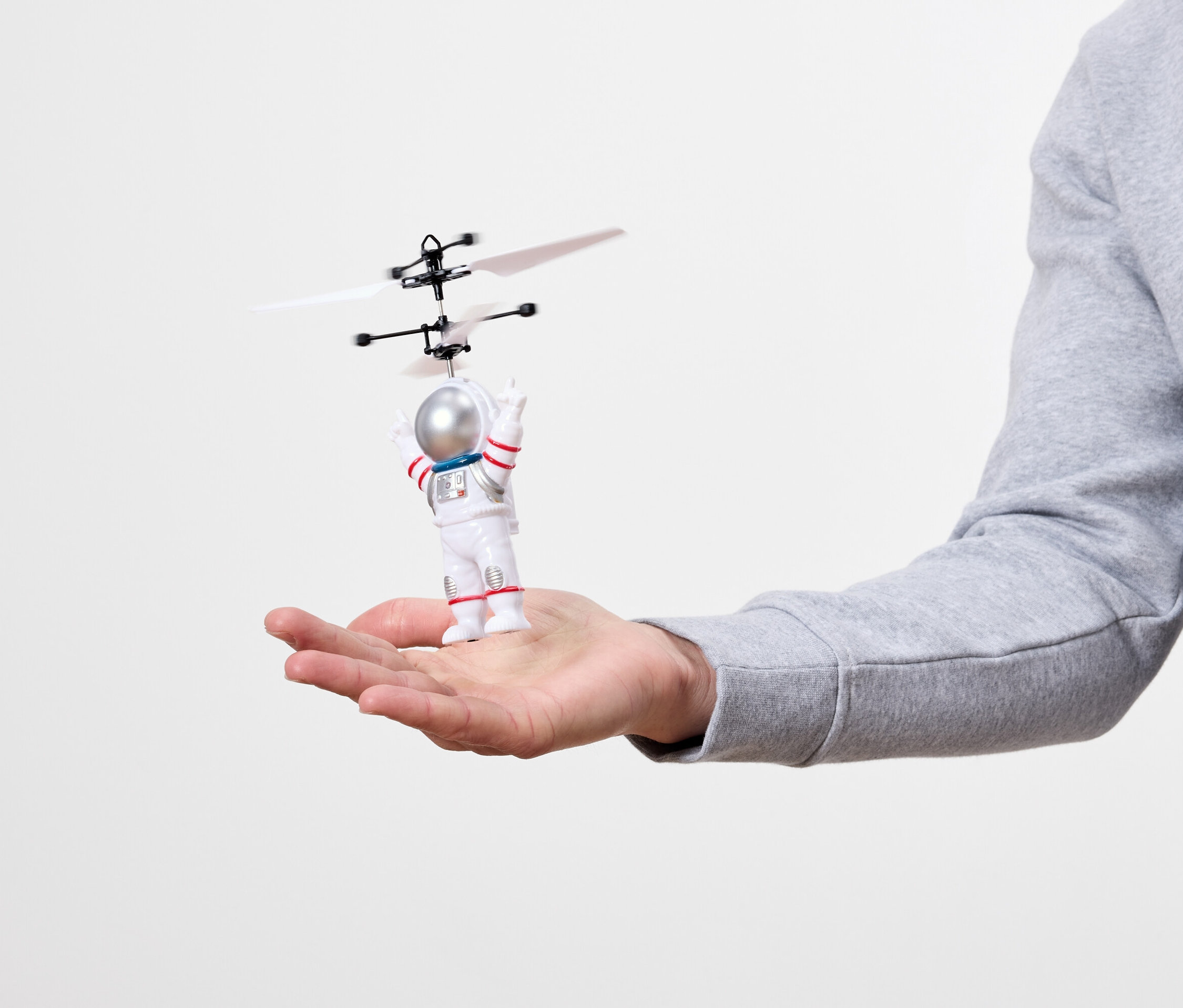 Auf einer Handfläche liegt ein kleines Astronautenspielzeug mit einem Propeller über dem Kopf.