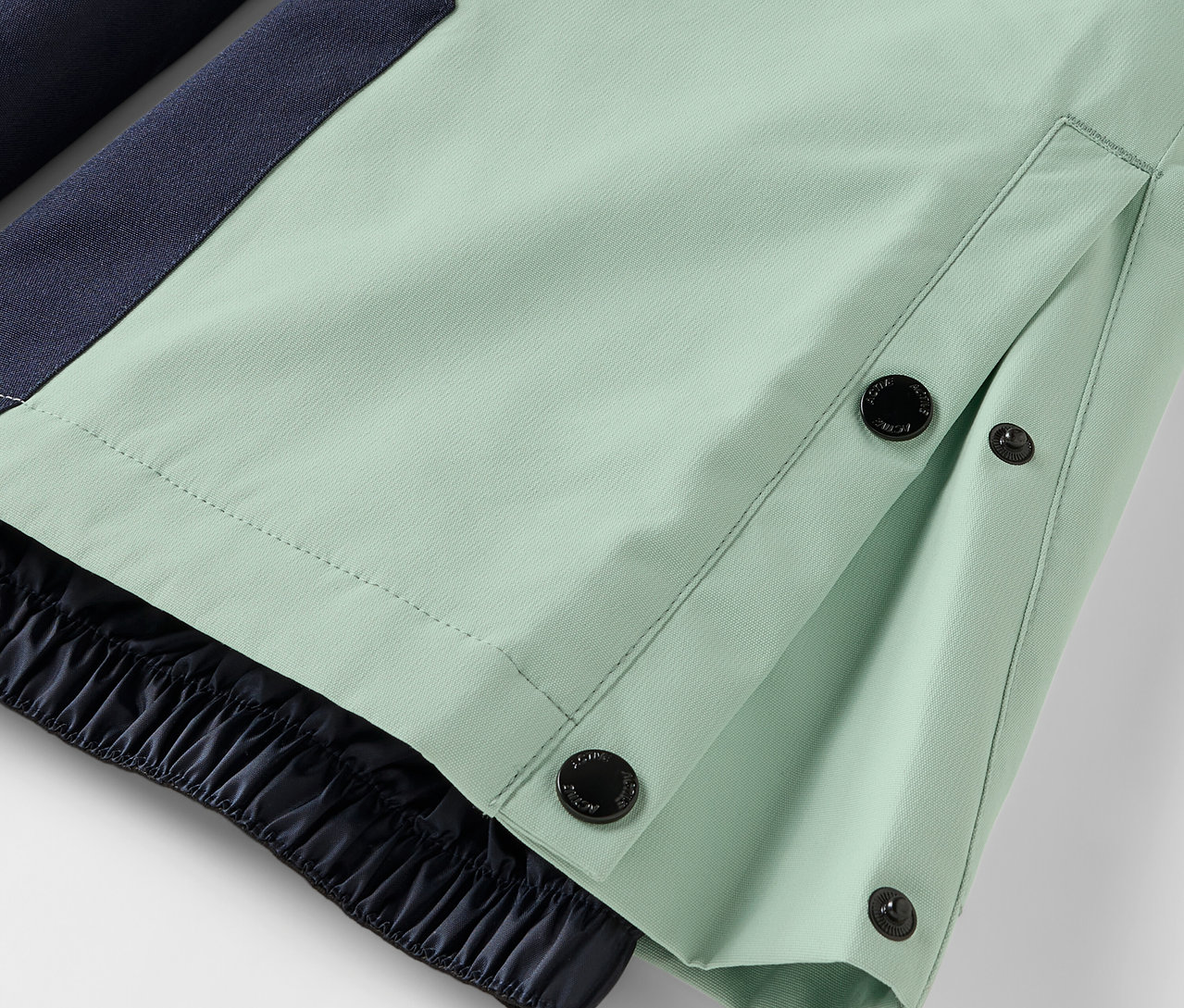 Detail einer hellgrünen Hose mit Knopfverschluss und elastischem Saum.