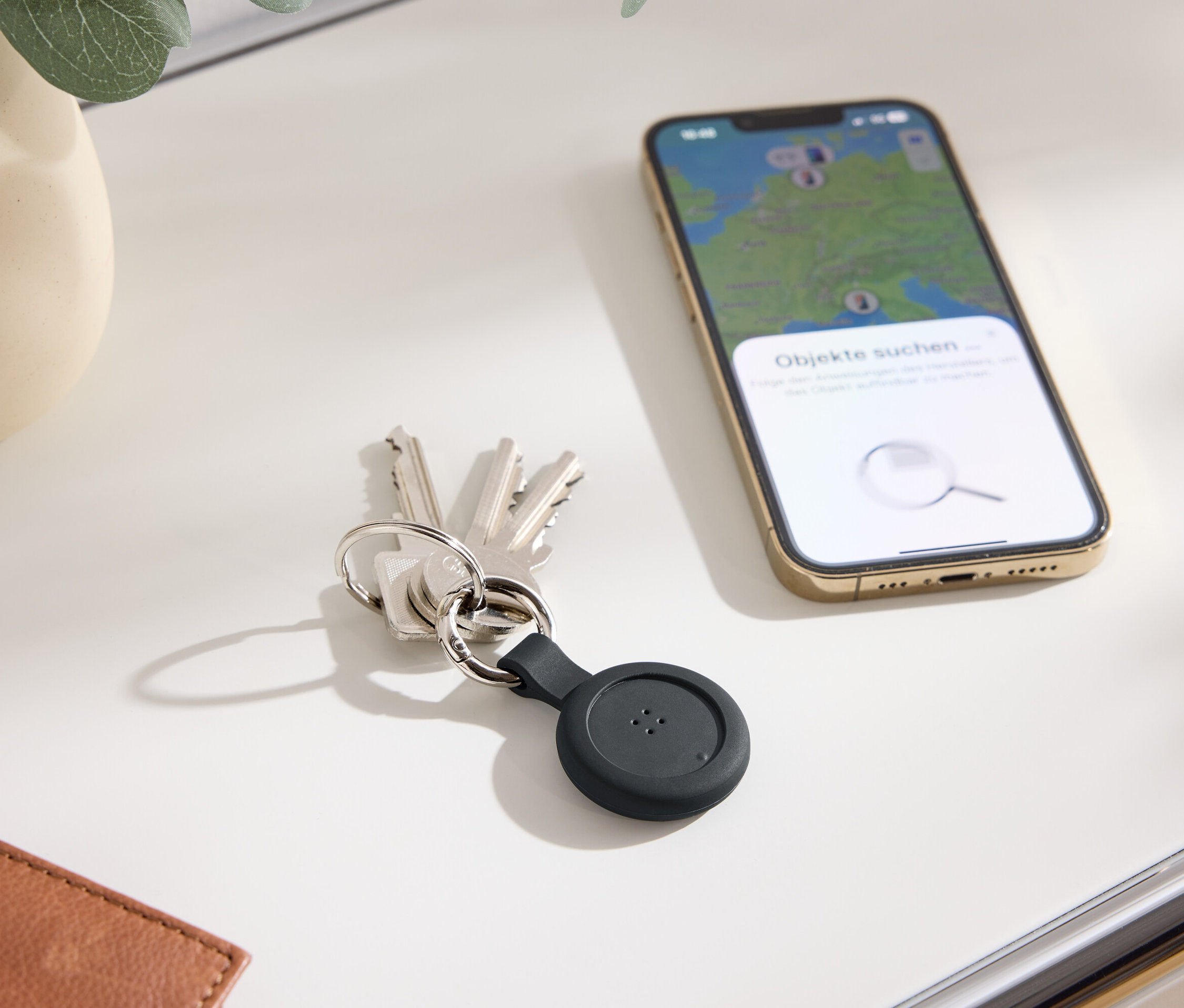 Schlüssel mit schwarzem Tracker und ein Handy mit einer Karte auf dem Display liegen auf einem Tisch.