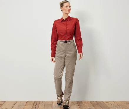 Frau trägt eine Outdoorhose mit Moskito-Schutz, ein braunes Hemd und Wanderschuhe.