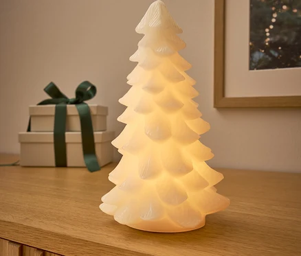 Auf einer Holzkommode stehen ein leuchtender Baum, dahinter zwei Geschenke mit dunkelgrünem Band und ein Bild mit Weihnachtsmotiv.