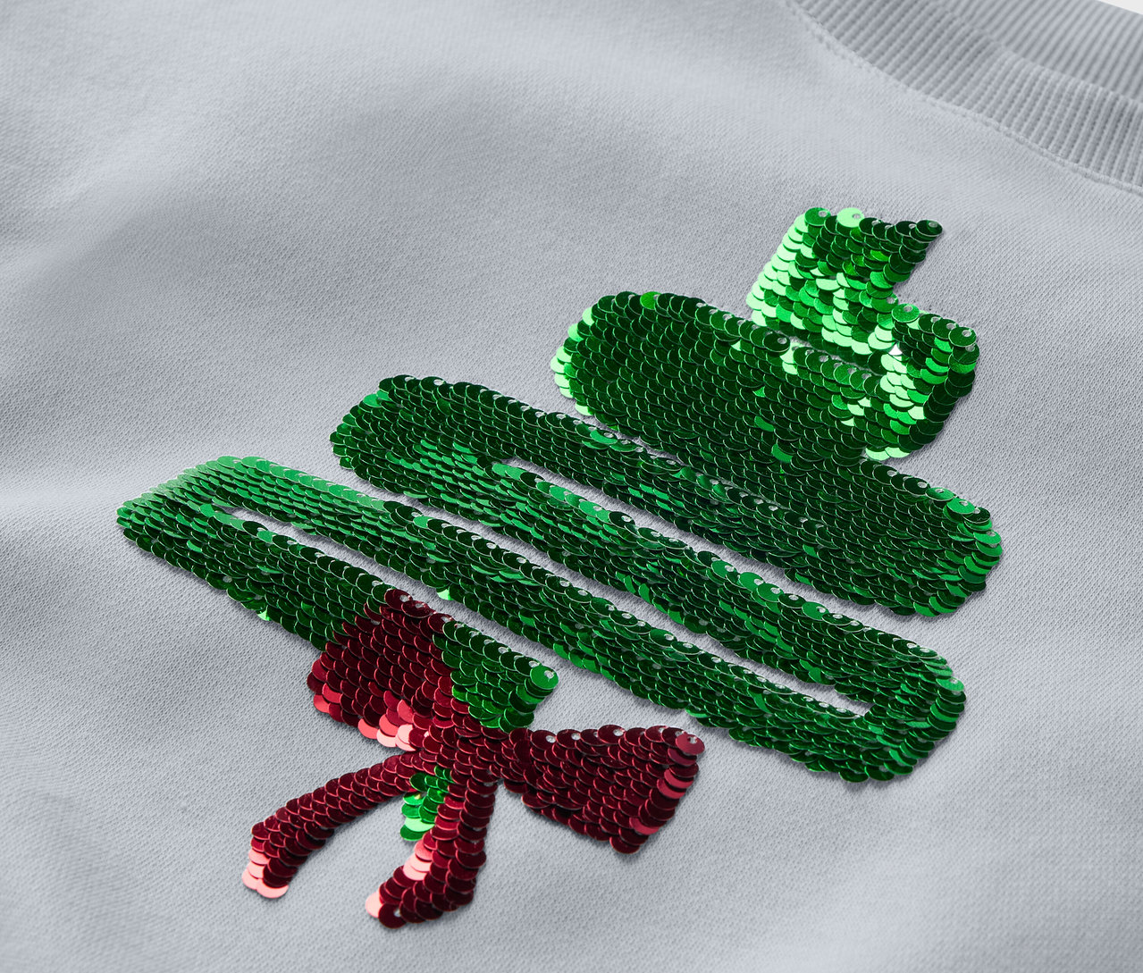 Detail eines grauen Sweatshirts mit Pailletten-Weihnachtsbaum.