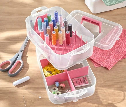 Geöffneter Utensilienbox, Kunststoff mit Fäden, Schere, Nadeln und Nähmaschine auf einem Tisch.