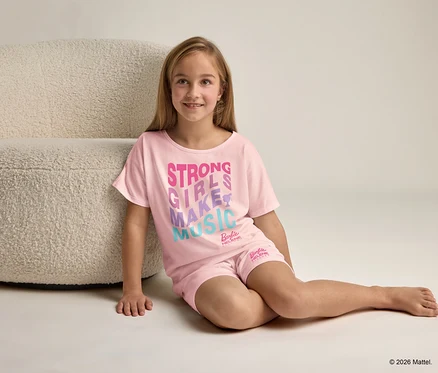 Ein Mädchen sitzt neben einem Sessel und trägt einen rosa Schlafanzug mit der Aufschrift "Strong Girls Make Music".