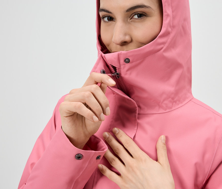 Frau schließt Reißverschluss einer pinkfarbenen Regenjacke mit Kapuze.