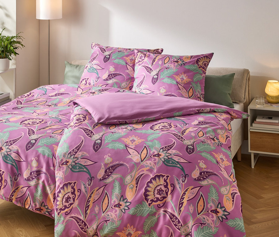 Lila Bettwäsche mit Blumenmuster auf einem gemachtem Bett.