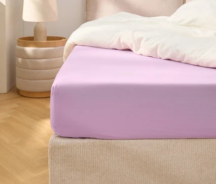Nahaufnahme eines lila Spannbetttuchs auf einem Bett mit weißer Bettdecke.