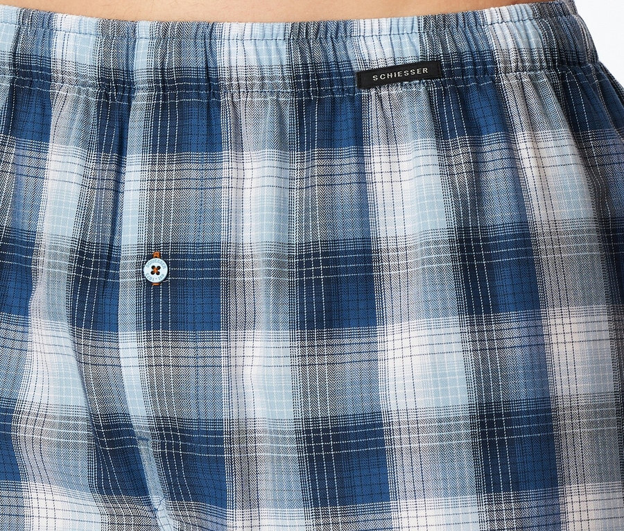 Nahaufnahme der karierten SCHIESSER Boxershorts in Blau- und Weißtönen mit einem Knopf und einem schwarzen Bund.