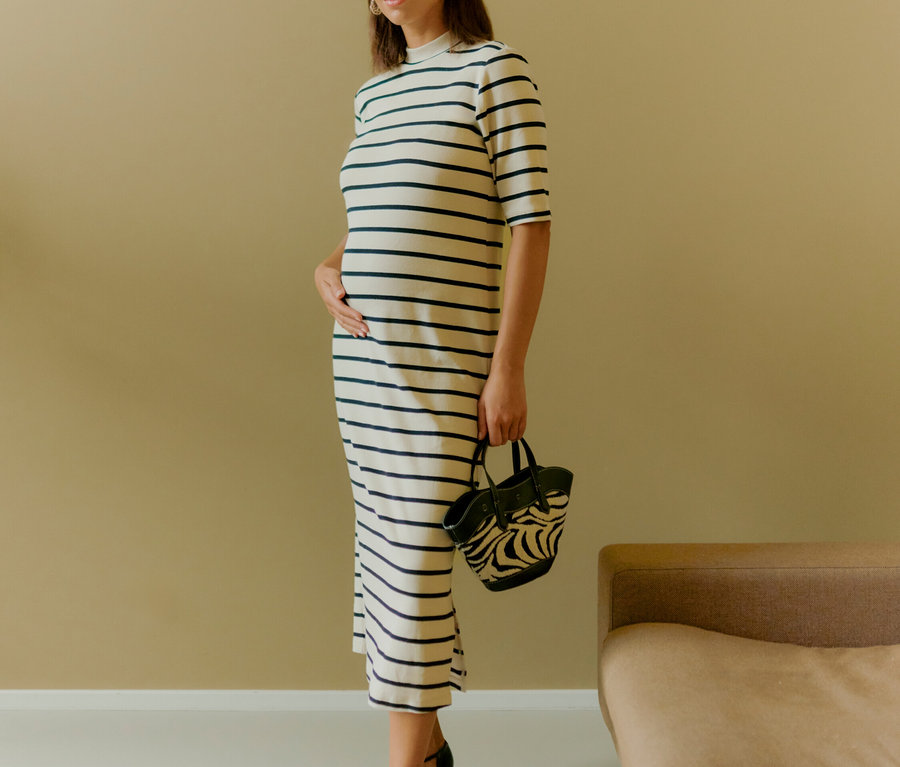 Eine Frau steht und hält eine Zebra-Handtasche. Sie trägt ein gestreiftes Kleid und schwarze Schuhe.