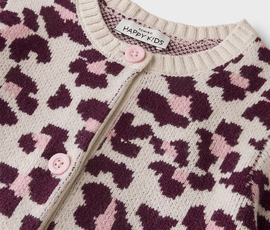 Nahaufnahme einer cremefarbenen Strickjacke mit Leopardenmuster in Dunkelrosa und Hellrosa. Sie hat hellrosa Knöpfe und ein „Happy Kids“-Etikett am Kragen.