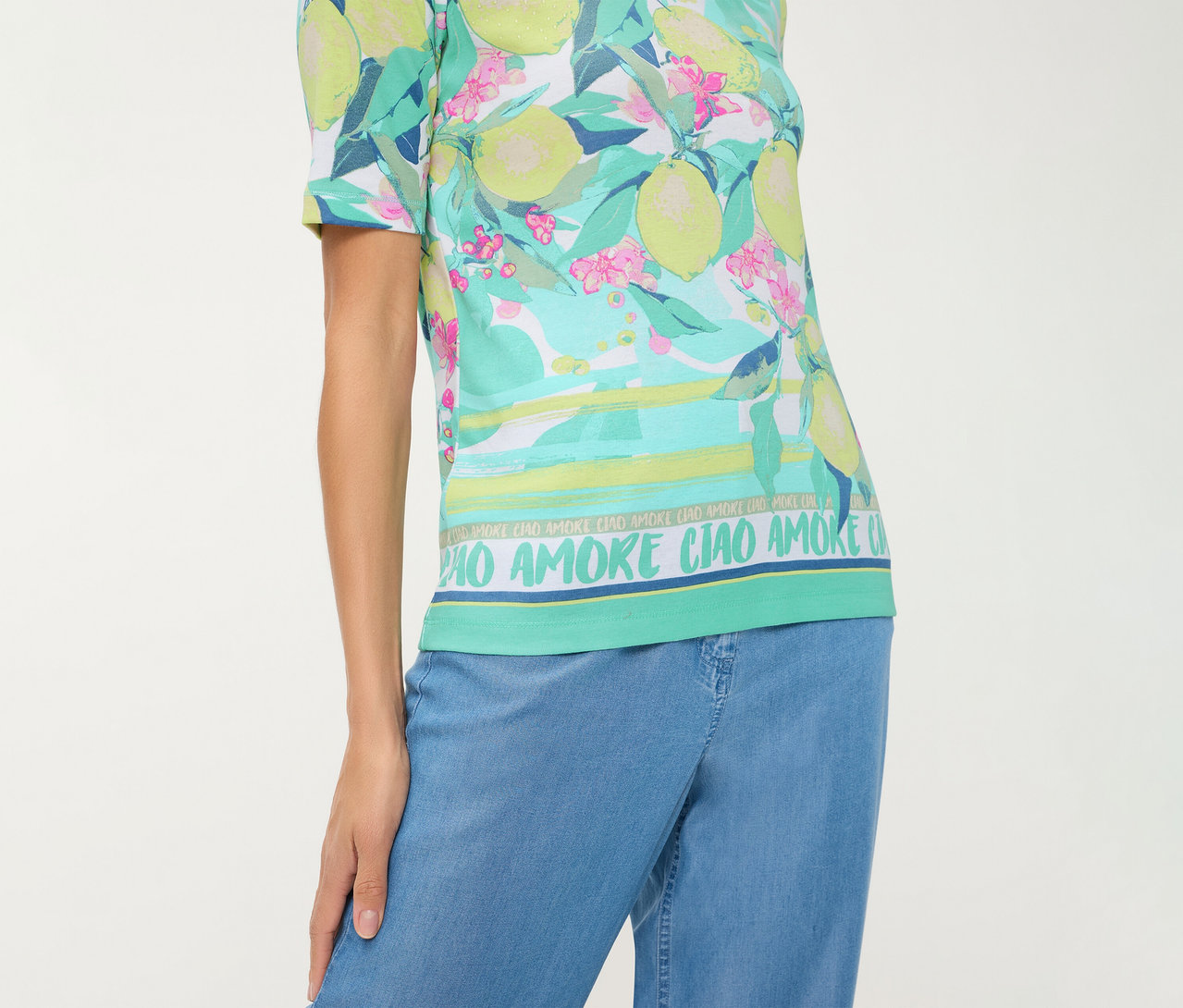 Person trägt ein Olsen T-Shirt mit Zitronen- und Blumenmuster, horizontalen Streifen und dem Schriftzug "CIAO AMORE", dazu eine blaue Hose.