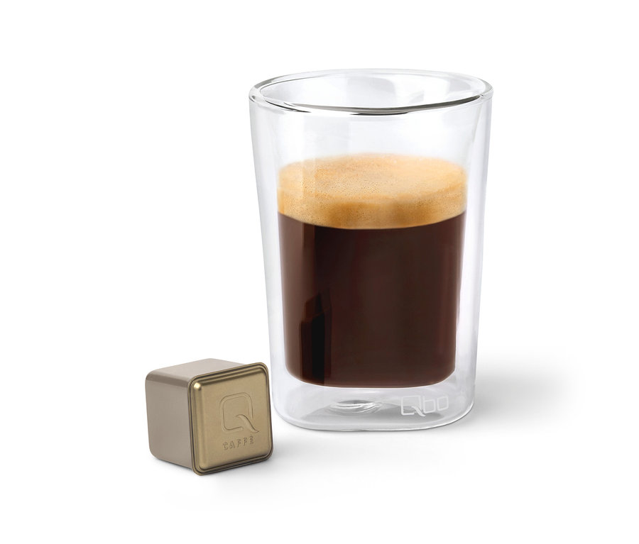 Eine Qbo Caffè JABANA YIRGA Kapsel neben einem Glas Kaffee.
