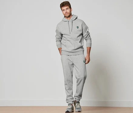 Mann steht und trägt einen grau melierten Hoodie und eine Jogginghose.