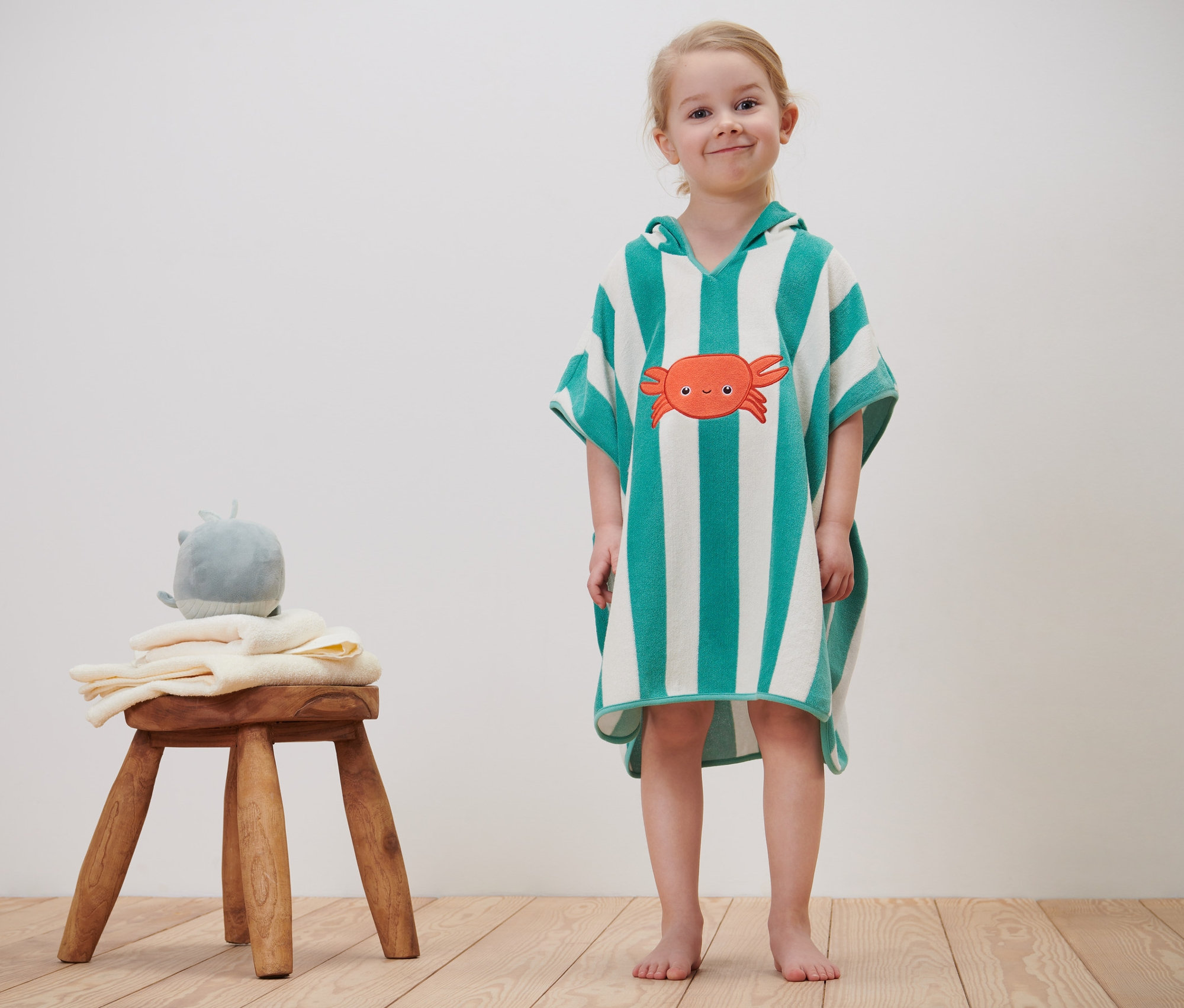 Mädchen trägt Baby-und-Kinder-Frottierponcho mit Krabbenmuster.