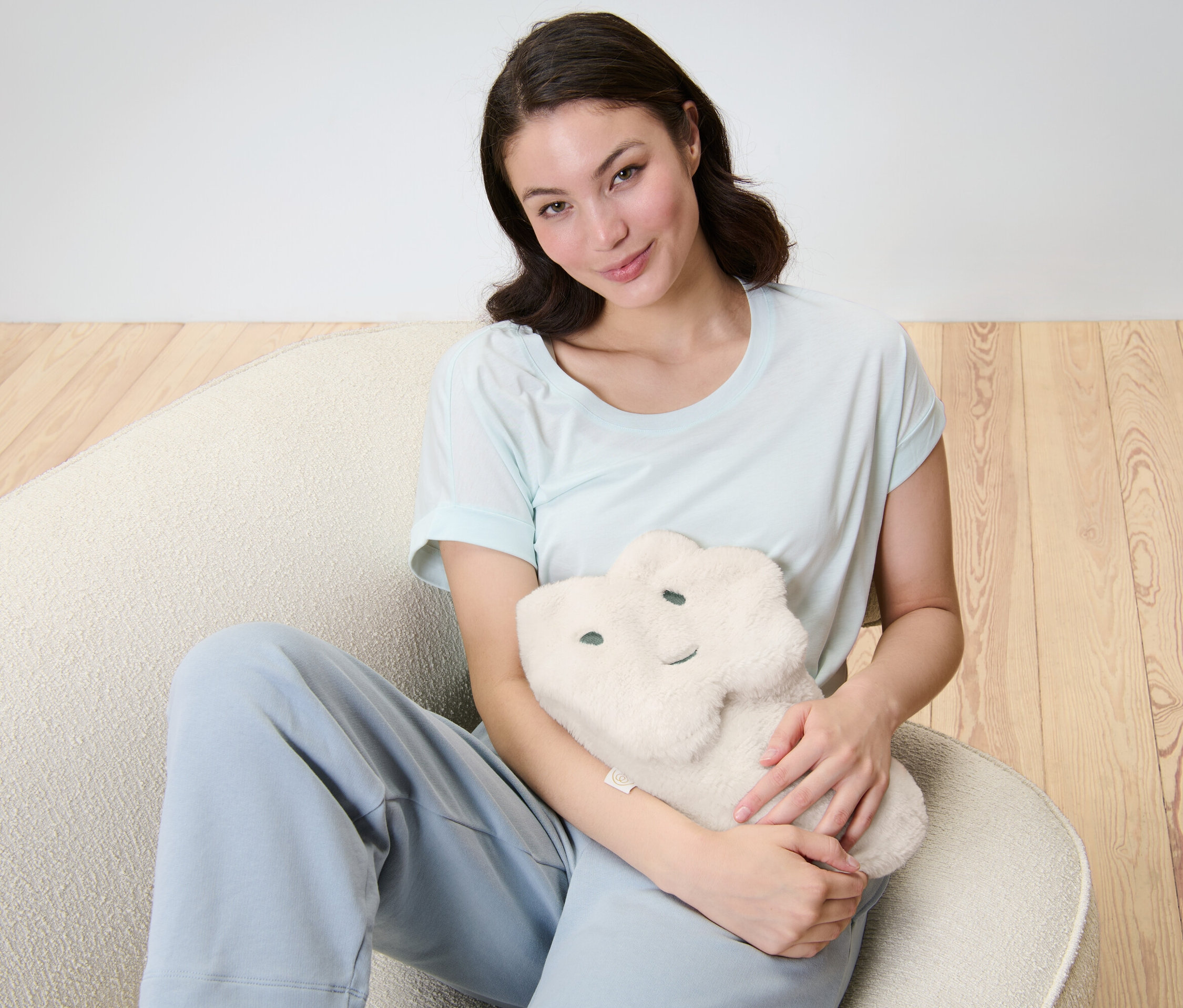 Frau sitzt und umarmt Wärmflasche »Wolke«.